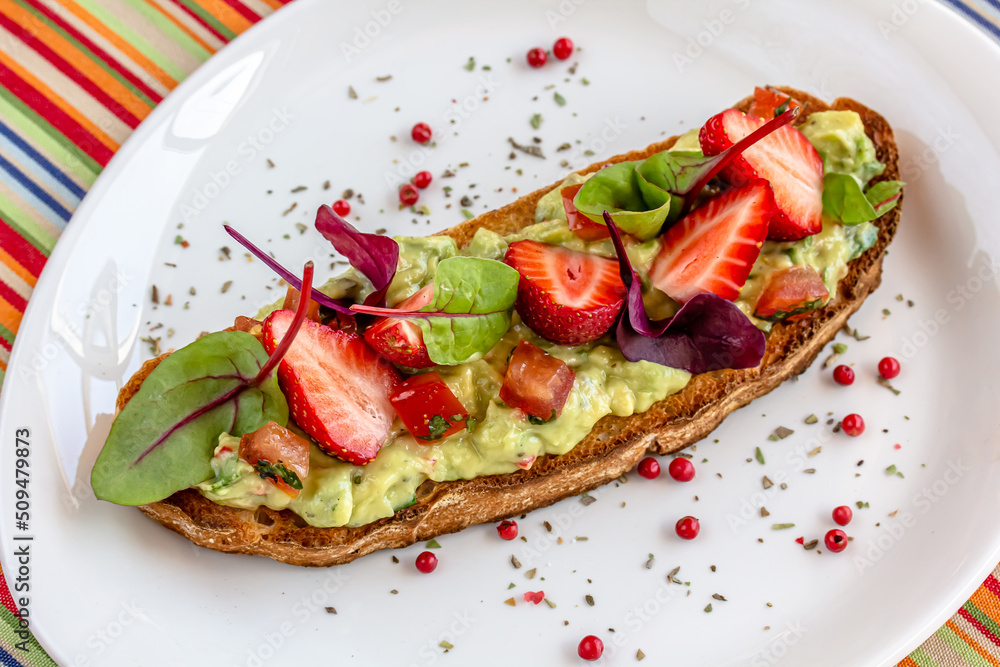 Keto diet avocado toast with strawberries, soft cheese, sesame seeds and herbs. healthy Breakfast or lunch. sandwich recipe mix media. top view, selective focus
