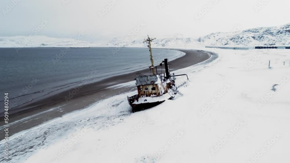 View of the old wrecked fishing vessels that sank on the seashore during the snowy winter season. A wrecked boat off the sandy coast View of the old wrecked fishing vessels that sank on the seashore during the snowy winter season. A wrecked boat off the sandy coast
