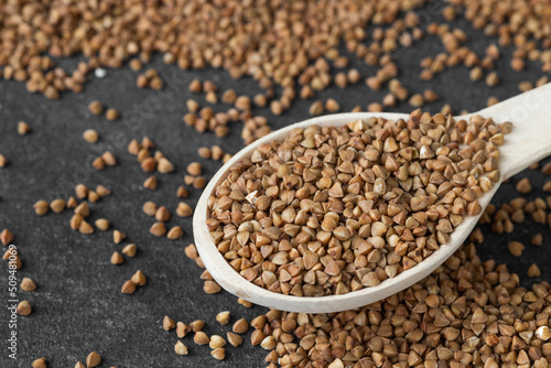 Uncooked buckwheat in a spoon on dark old boards. Buckwheat is used for cooking.