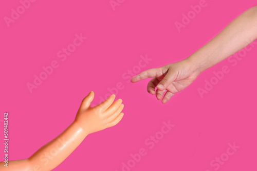 Child's hand extends a finger to the hand of a plastic doll. The Creation of Adam.