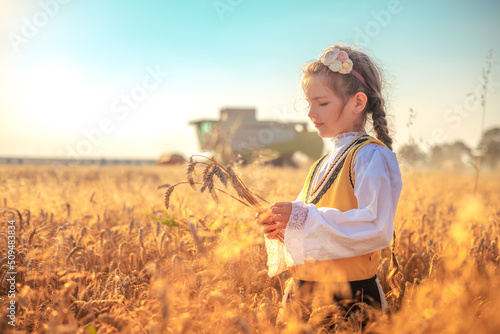 Fotografia Young girl with traditional Bulgarian folklore costume at the agricultural wheat