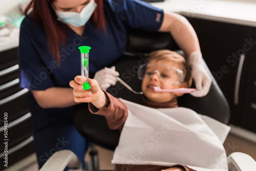 Smiling little boy in dentists chair, being educated about proper tooth-brushing by her paediatric dentist. Early prevention, raising awareness, oral hygiene demonstration concept.