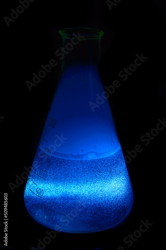 Erlenmeyer flask with a blue liquid on a black background - close up photo. Background picture for your desktop.