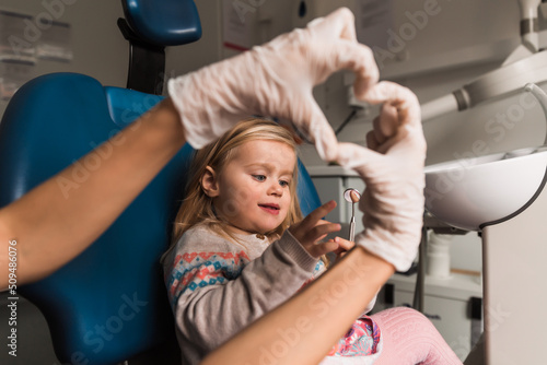 smiling little girl in dentist chair, dentist showing heart with hands