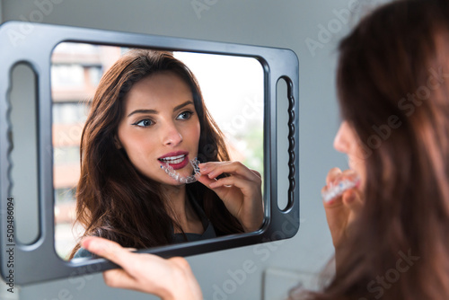 Close up of a woman in front of a mirror  putting on invisible plastic teeth aligners or braces. Beautiful and healthy smile. Teeth whitening.