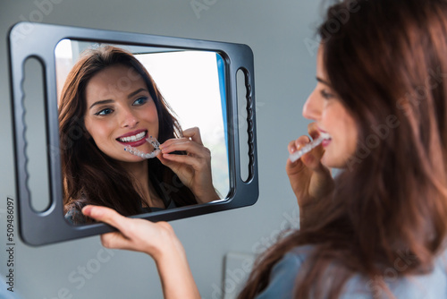Young woman wearing plastic form for teeth alignment or whitening, looking to the mirror