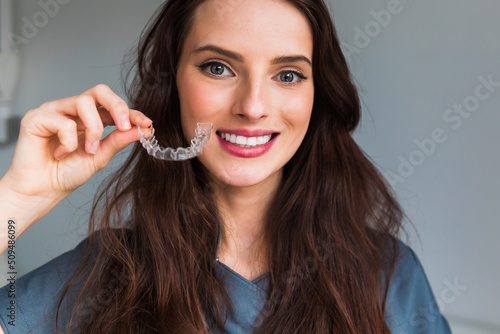 Young beautiful  woman holding dental aligner orthodontic to teeth correction with happy face near mouth photo