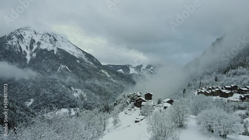 Winter mountains covered in snow and forest with wooden houses on the mountain top village above the clouds drone panorama.