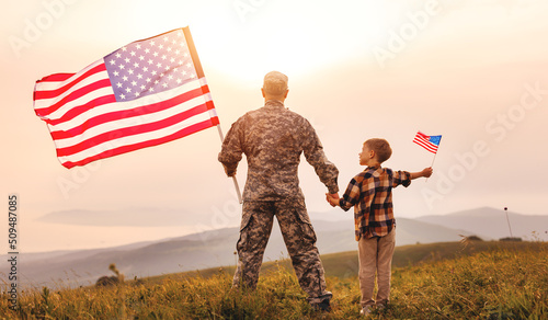 Rear view of military man father holding   son\'s hand   with american flag   and enjoying amazing summer nature view on sunny day, happy male soldier dad reunited with son after US army