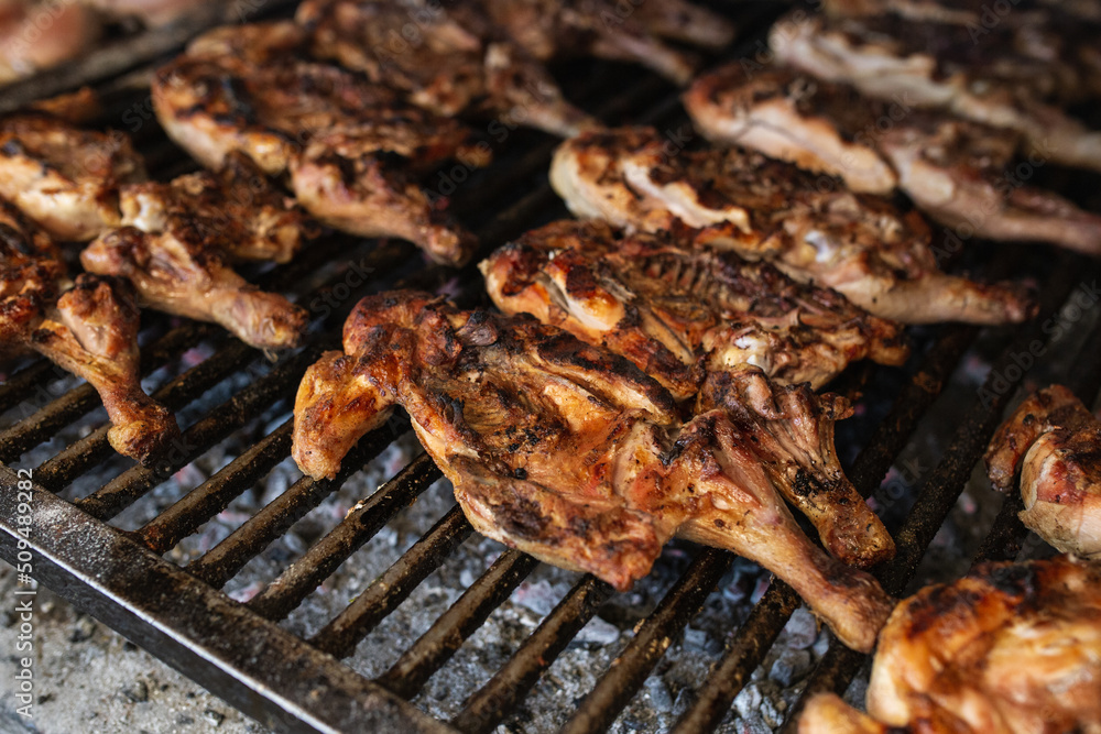 seasoned chickens cooking on the coals on a metal grill seasoned chickens cooking on the coals on a metal grill