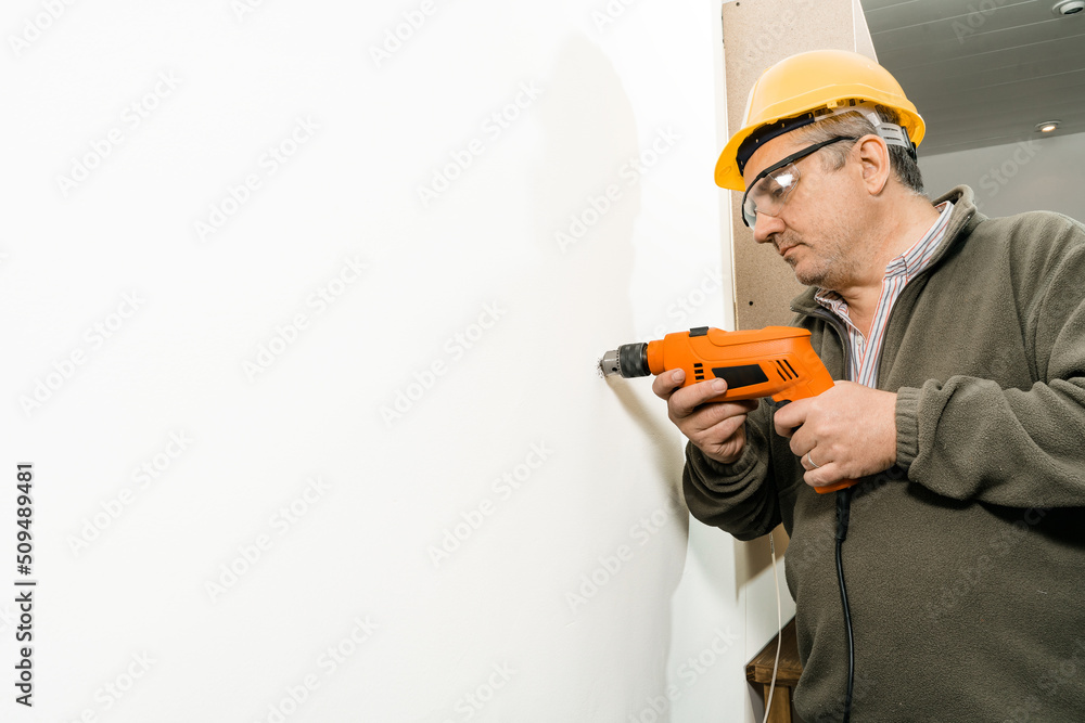 Worker drilling a hole with a drill on a white wall. Copy space. Worker drilling a hole with a drill on a white wall. Copy space.