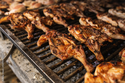 seasoned chickens cooking on the coals on a metal grill