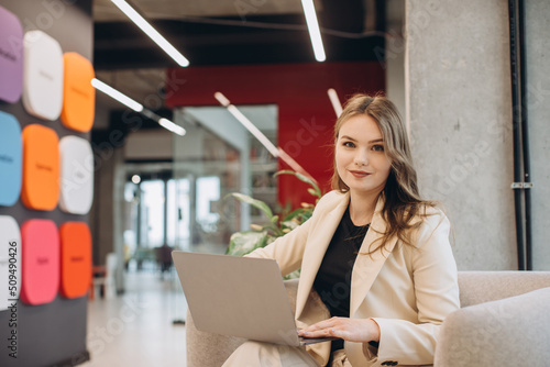 Young female entrepreneur using laptop in modern office corridor