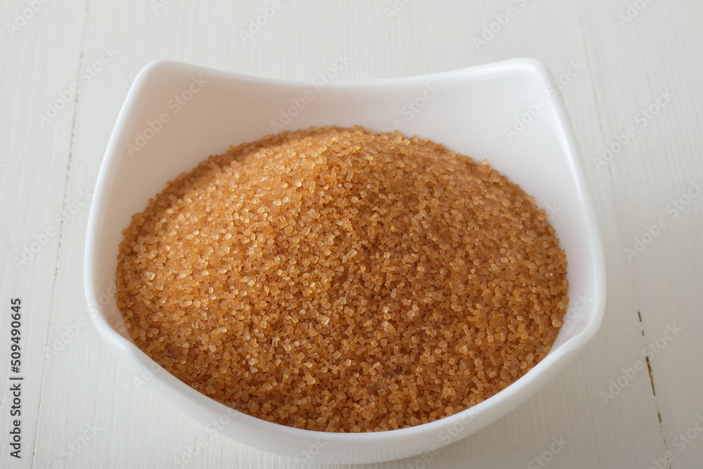 Granulated cane sugar in porcelain bowl on a white wooden table. Closeup, no people. Granulated cane sugar in porcelain bowl on a white wooden table. Closeup, no people.