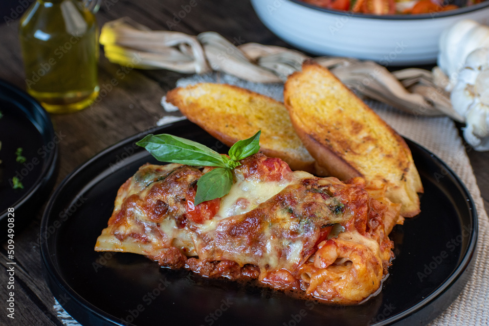 Meat lasagna with basil and bread in an elegant black plate