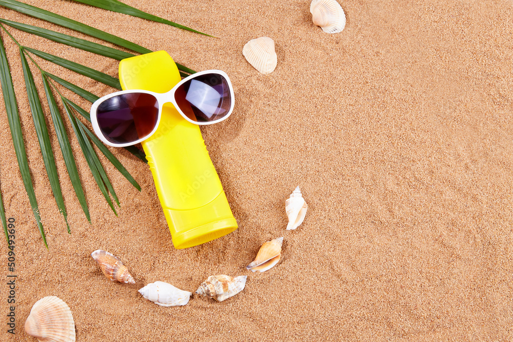 Summer background. Sunscreen, sunglasses, shells and palm leaves on the sand on the beach. The concept of summer holidays, protection from the sun. Top view. Mock up