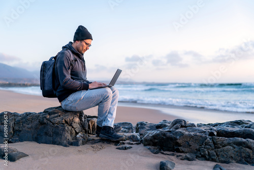 digital nomad working on his laptop outdoors from the beach at sunset photo