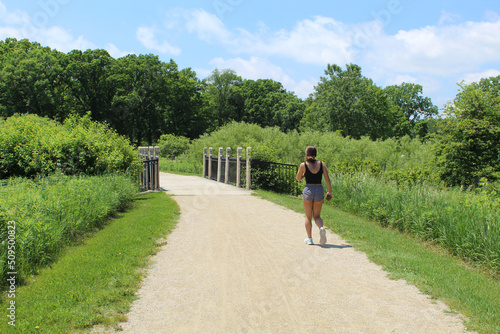 Woman in shorts holding a mobile phone about to walk across a bridge at Middlefork Savanna in Lake Forest, Illinois