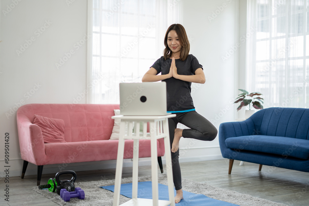 Beautiful Asian young girl doing Yoga,follow online trainer in laptop.Attractive female in sportswear spend leisure activity time to workout for health by follow online instruction on laptop at home. Beautiful Asian young girl doing Yoga,follow online trainer in laptop.Attractive female in sportswear spend leisure activity time to workout for health by follow online instruction on laptop at home.