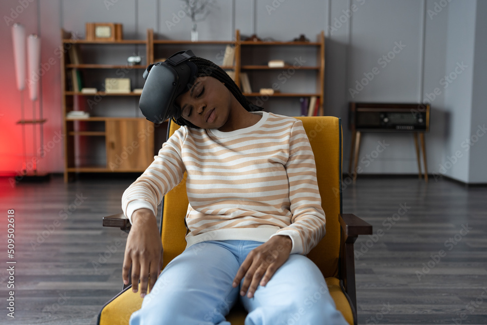 Tired african american female wearing virtual reality goggles sleeping in armchair at home after using VR technology for too long. Girl sleeping. Cybersickness in virtual and augmented reality