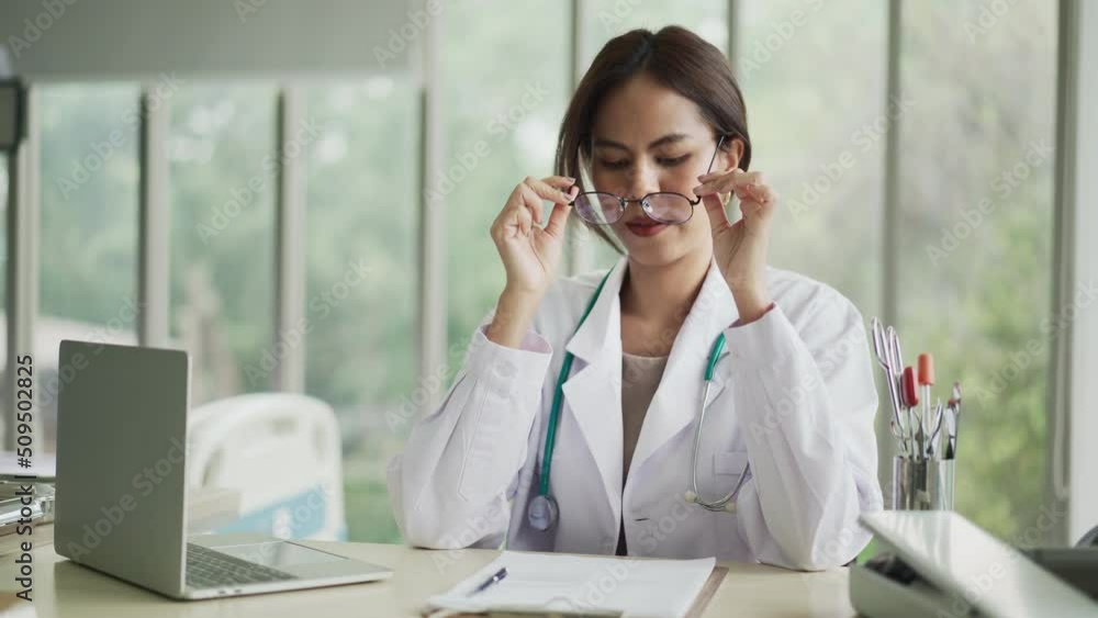 young female doctor typing on laptop and rubbing eyes sitting at desk in office, Upset young female doctor feeling tension,Tired doctor. young female doctor typing on laptop and rubbing eyes sitting at desk in office, Upset young female doctor feeling tension,Tired doctor.