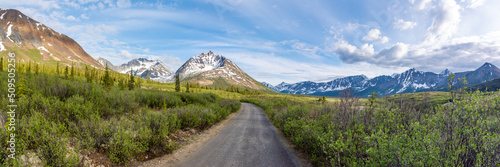 Panoramic mountain views in northern Canada, Yukon Territory during summer. Dirt road, highway leading towards iconic, epic Canadian mountain view in panorama view. 