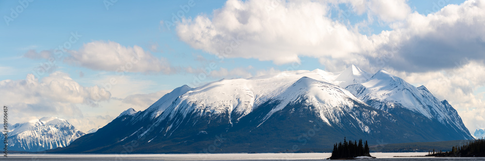 Panoramic shot of snow capped mountain view scenery seen in northern British Columbia during spring time with blue sky day and clouds.