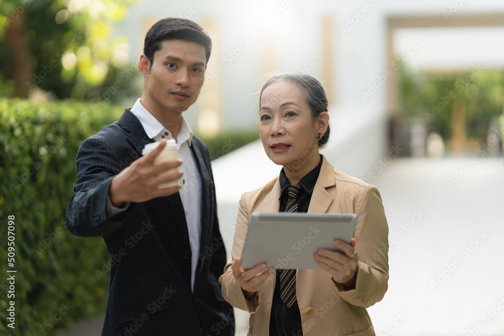 Portrait of Asian Senior Business woman and young business man discussing about project by digital tablet. Account and Finance concept.