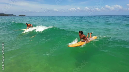 Aerial view group of Asian woman surfer paddling surfboard and riding the wave in the sea at tropical beach. Female friends enjoy outdoor activity lifestyle and water sport surfing on summer vacation