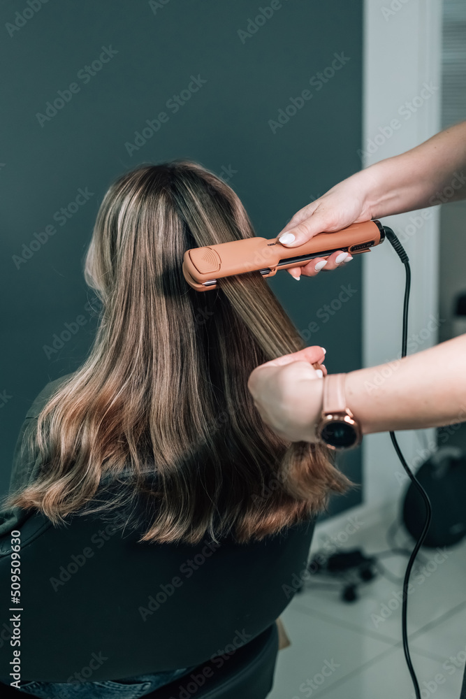 Naklejka premium Close up Pulling strands of hair with professional ultrasonic iron tool. Spa care. Keratin straightening and restoration.
