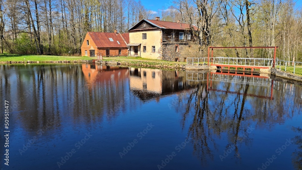 Water mill on the shore of lake and its reflection on the surface of the water in Latvian village of Garsenes in April 2022 Water mill on the shore of lake and its reflection on the surface of the water in Latvian village of Garsenes in April 2022