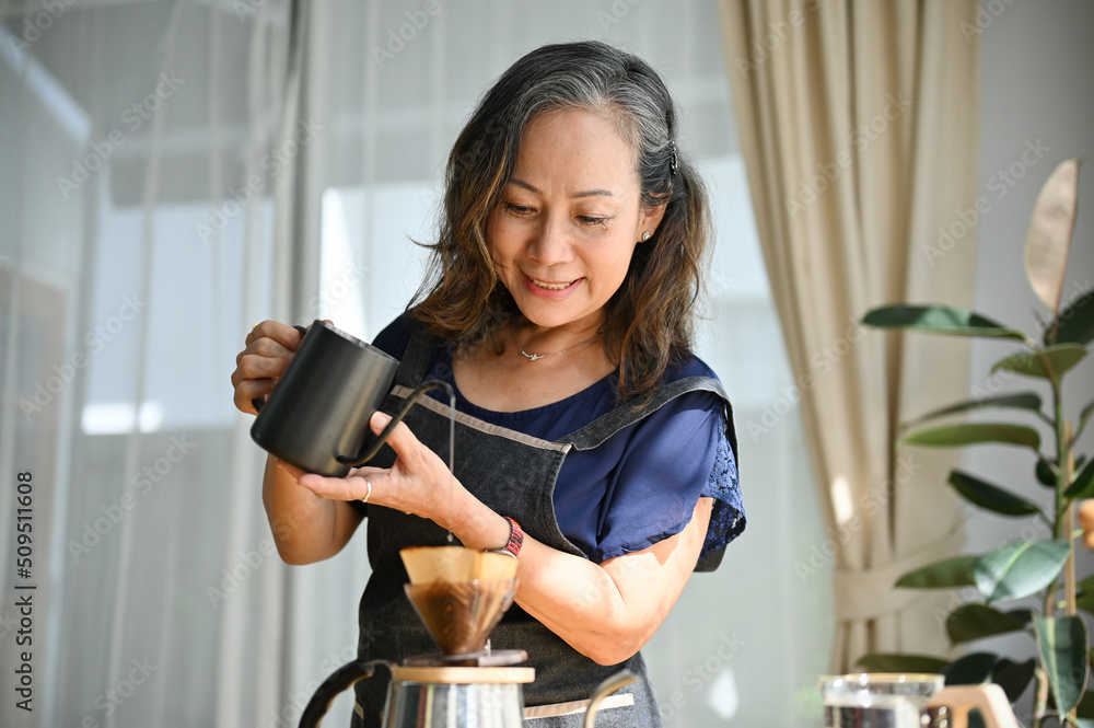 Charming asian aged woman making a morning coffee, pouring hot water into a coffee kettle