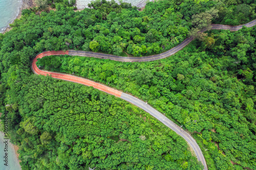 Top view of countryside road passing through the green forrest and mountain