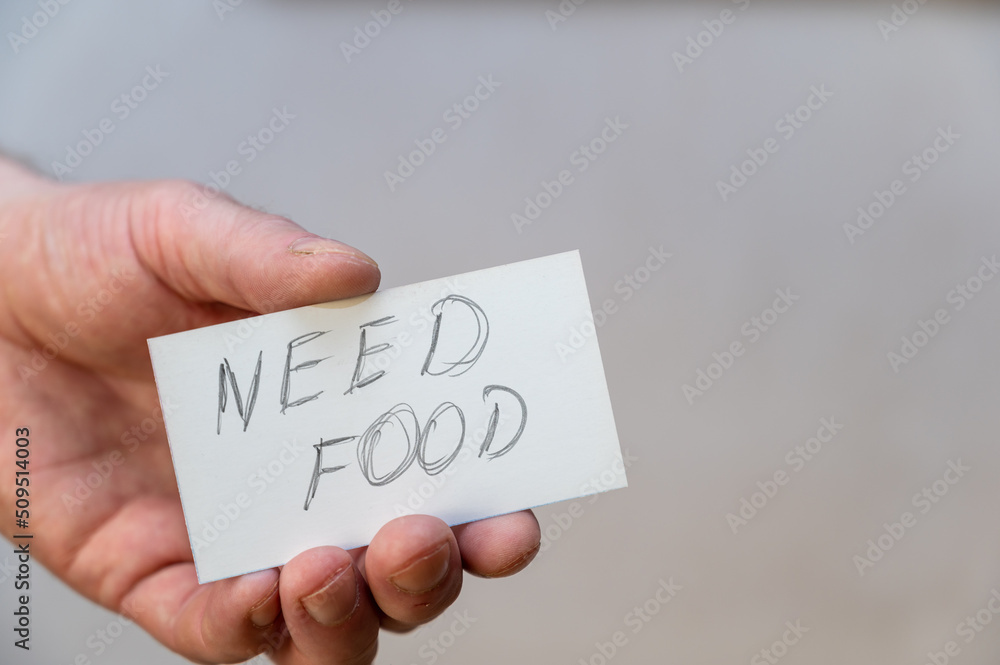 Need food. Words written in jagged letters. A man's hand holds a white paper rectangle with text against a gray background. Need food. Words written in jagged letters. A man's hand holds a white paper rectangle with text against a gray background.