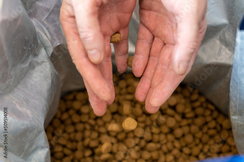 Empty palms over a bag of dog food. Pellets of dog food spill out of the man's hands. The hands of a middle-aged man. The food falls into an open bag. Blurred motion. Close-up. Selective focus.