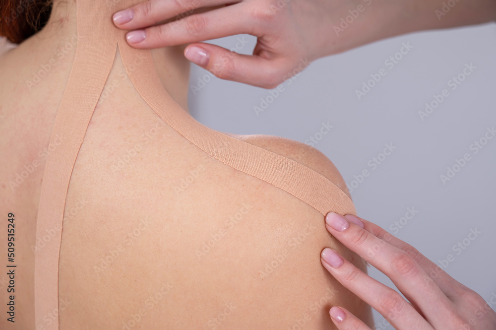 Fototapeta premium Female doctor glues kinesio tapes on the patient's shoulder. 