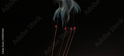 Aromatic agarbathi, agarbatti or Incense sticks smoldering in room with smoke and aroma. Isolated in dark black background with copy space. It used in asian religious prayer. Closeup macro side view. photo