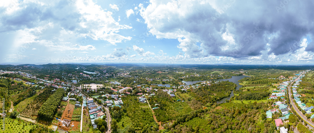 Fototapeta premium Aerial panorama view of National Route 14 in Kien Duc town, Dac Nong province, Vietnam with hilly landscape, sparse population around the roads and Dak R'tang lake.