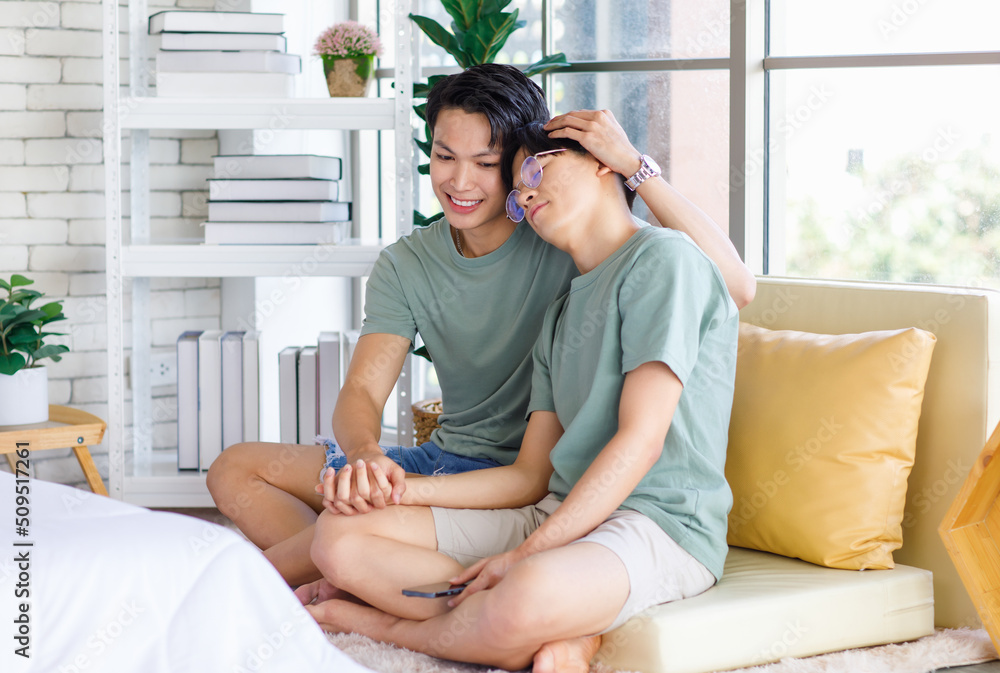 Two Asian young handsome pride male gay men lover couple partner sitting smiling together on cozy sofa in bedroom holding hands cuddling hugging touching head showing LGBTQ love equality relationship Two Asian young handsome pride male gay men lover couple partner sitting smiling together on cozy sofa in bedroom holding hands cuddling hugging touching head showing LGBTQ love equality relationship