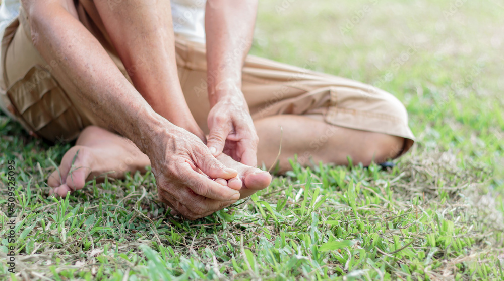 Asian old man suffering from toe pain sitting on grass . Asian retired health problems Hands touch and massage while relieving pain, menopause Asian old man suffering from toe pain sitting on grass . Asian retired health problems Hands touch and massage while relieving pain, menopause