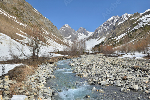 fresh river crossing the alpine valley on a bed of pebbles and mountains still snowy in spring