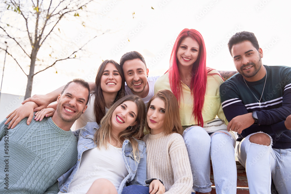 Fototapeta premium Group of friends smiling at the camera while sitting together on a bench. Concept of friendship and positivity.