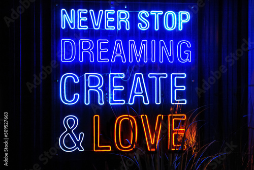 Blue and Red neon light lettering "Never stop dreaming create and love" in dark, restaurant or cafe. Front view, closeup.