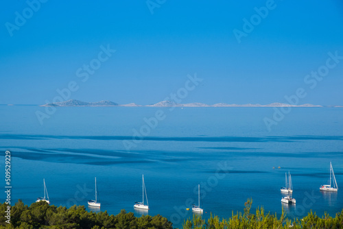 Panoramic view on Kosirina lagoon on Murter island in Croatia, anchored sailing boats and yachts on blue sea, Kornati archipelago in background photo