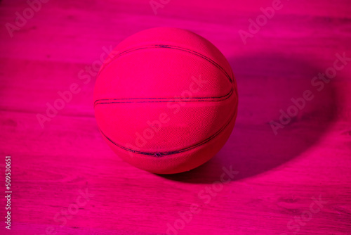 Basketball on wooden floor in room with bright colored light
