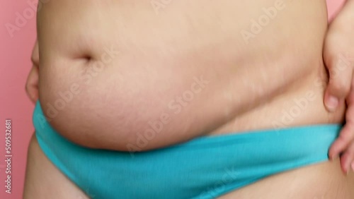 Closeup confident, playful adipose woman with excess weight in blue panties shakes fat on big stomach. Excess weight and body volume problem. The fats on belly while dancing and bouncing. Need plastic