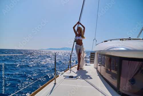 Foto Beautiful young blond woman in bikini standing on catamaran at sunny summer day