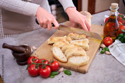 Woman slicing French bread baguette on wooden bread board