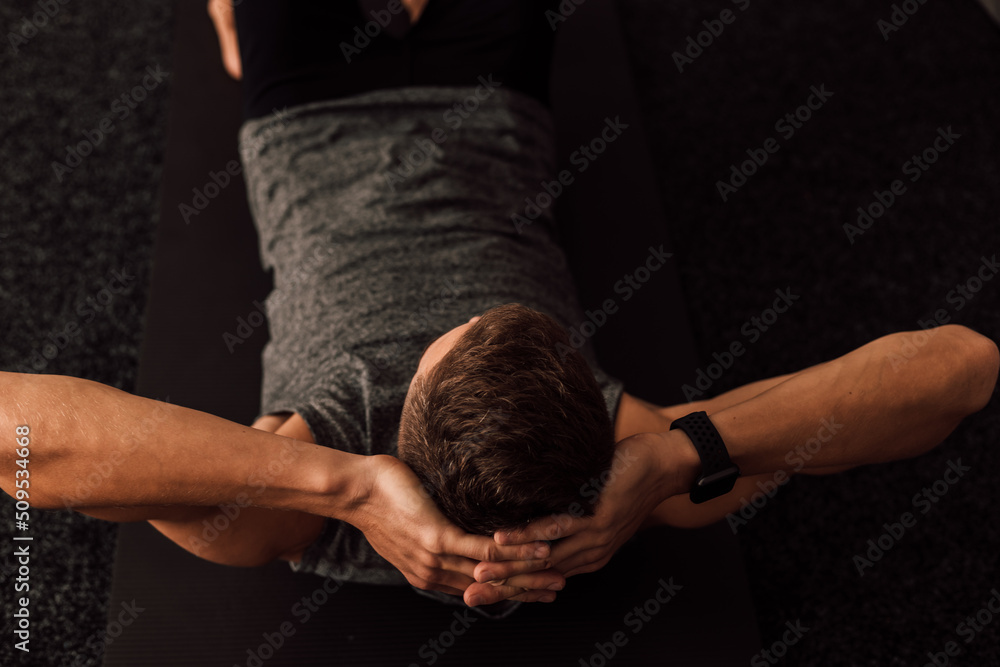 Strong male hands behind the head of an athlete who performs a sports exercise
