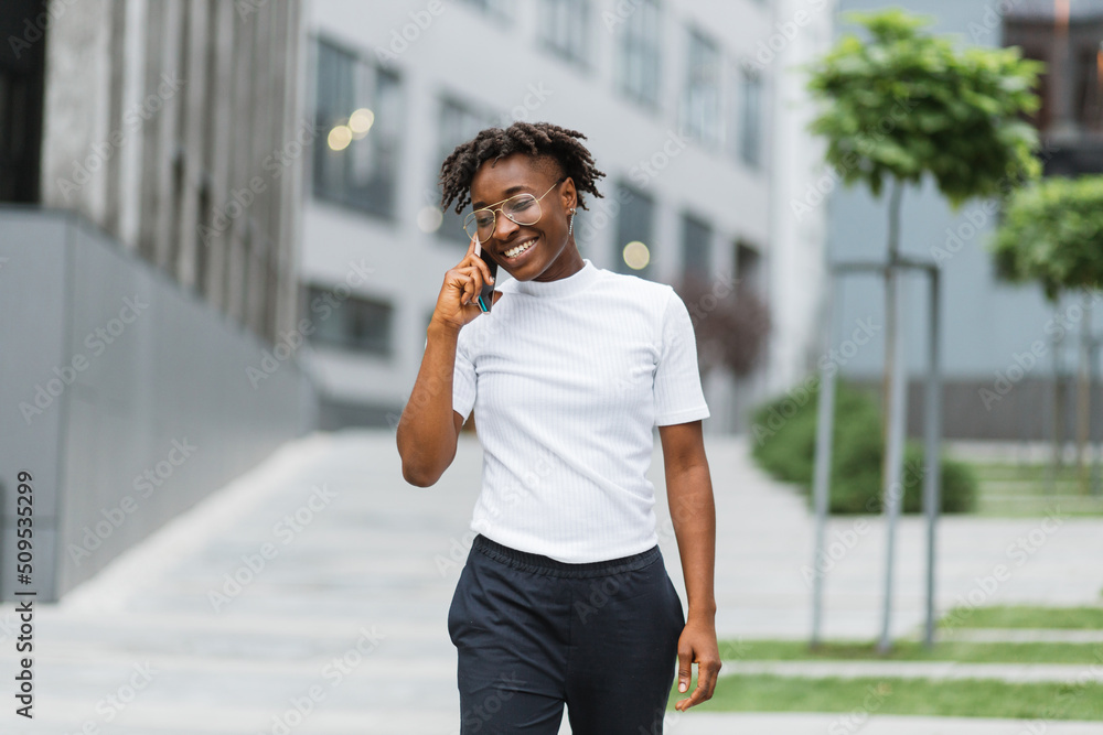 Front view portrait of attractive woman with mobile phone looking away and laughing on the city street. A pretty African american business woman talking on a cell phone at office building Front view portrait of attractive woman with mobile phone looking away and laughing on the city street. A pretty African american business woman talking on a cell phone at office building